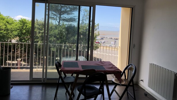 A balcony with a table and chairs, large sliding glass doors, a view of trees and a distant landscape.
