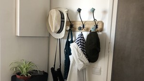A hallway with a coat rack holding hats and bags, a potted plant, and a door with a key lock.