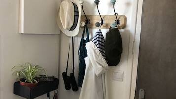A hallway with a coat rack holding hats and bags, a potted plant, and a door with a key lock.