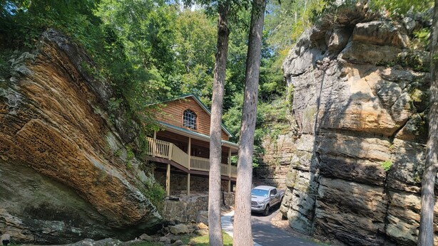A cabin with a porch, surrounded by rocky cliffs and trees.