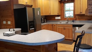 A kitchen with wooden cabinets, a stainless steel refrigerator, a sink, and a bar area with stools.