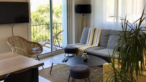Een woonkamer met een bank, fauteuils, een salontafel, een televisie en een balkon met uitzicht.