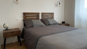 Een slaapkamer met een houten hoofdbord, een grijze spreideken, twee nachtkastjes en een wereldbol op één van de tafels.