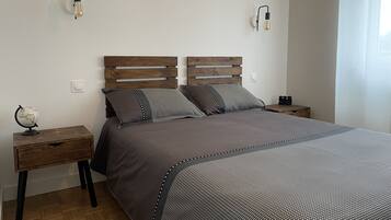 Une chambre à coucher avec une tête de lit en bois, une couvre-lit grise, deux tables de chevet et un globe sur l’une des tables.
