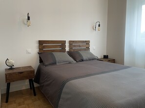 A bedroom with a wooden headboard, a grey bedspread, two bedside tables, and a globe on one table.