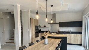 Een moderne keuken met een houten eiland, zwarte kastjes en een ingebouwde oven. Er is een zithoek met een houten tafel en zwarte stoelen.