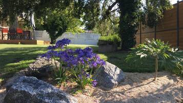 Un jardín con rocas grandes, flores moradas y una pequeña palmera.