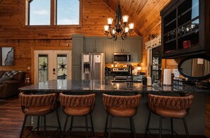 A kitchen with a central island, bar stools, and a chandelier.
