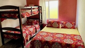 A dormitory room with bunk beds, a window with curtains, and a ceiling light fixture.