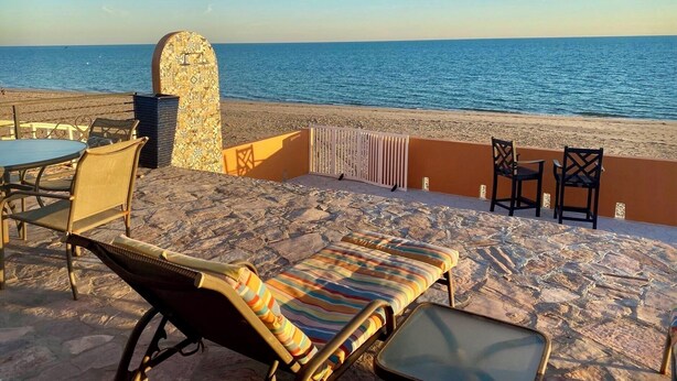 A beachside lounge with a view of the sea, featuring lounge chairs, a table, and a decorative wall.