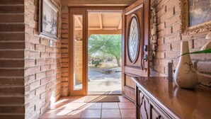 A hallway with brick walls, a wooden door, and a tiled floor leading to an outdoor area.