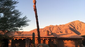 A house with a tiled roof, a palm tree, and a mountain in the background.