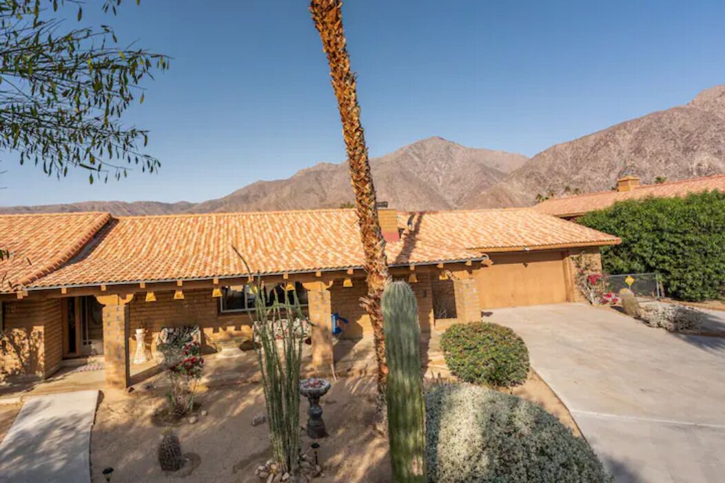Una casa con tetto a tegole, un giardino con cactus e montagne sullo sfondo.