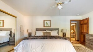 A bedroom with a large bed, two bedside tables, a ceiling fan, and a wooden wardrobe.