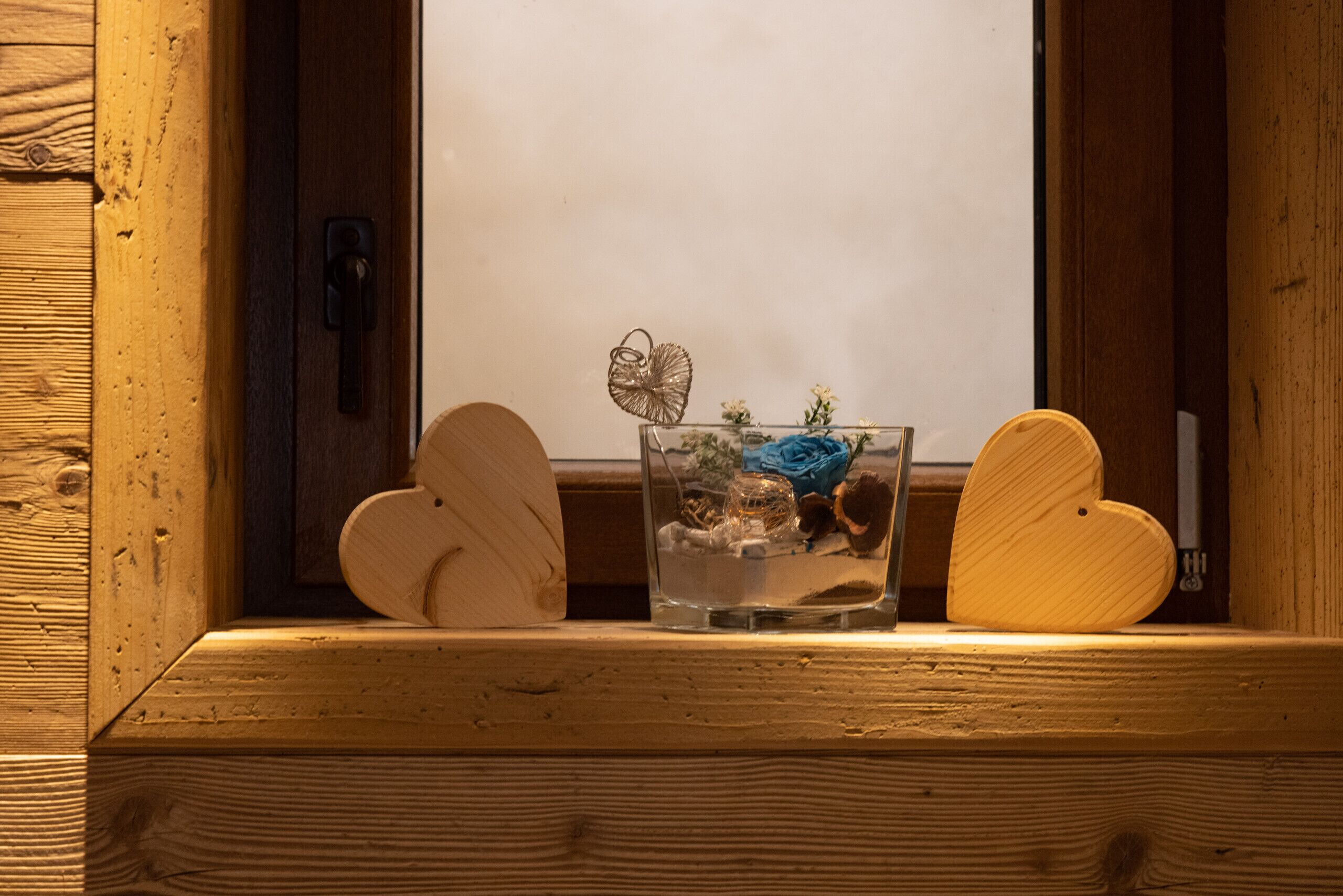 Un cadre de fenêtre en bois surmonté d’une table en verre, laquelle contient un objet décoratif et un objet en forme de cœur.