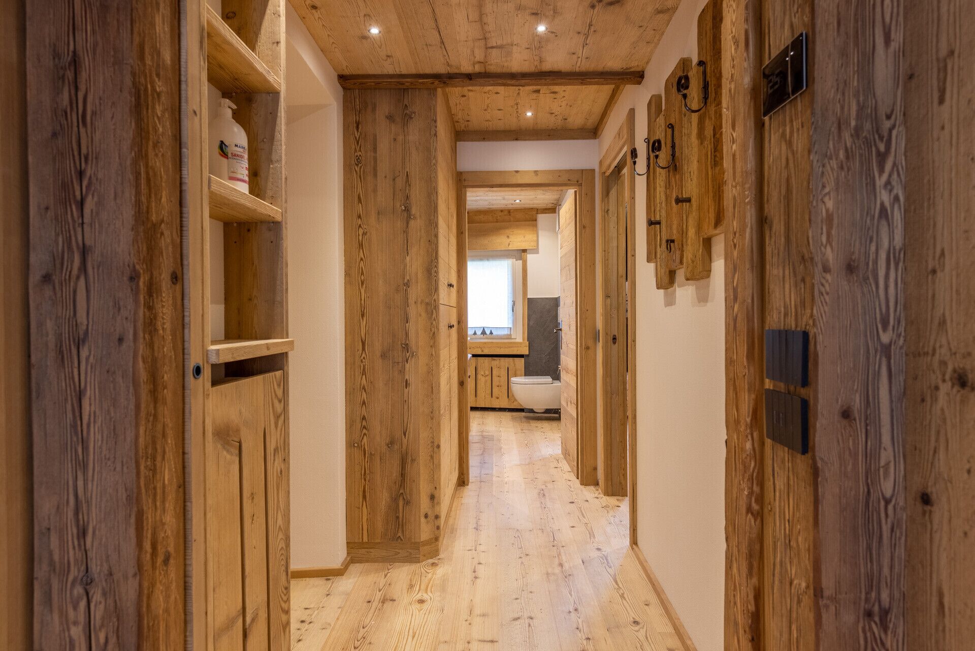 Ein Holzboden erstreckt sich durch einen Holzflur, mit einem Fenster und einer Toilette in der Ferne.