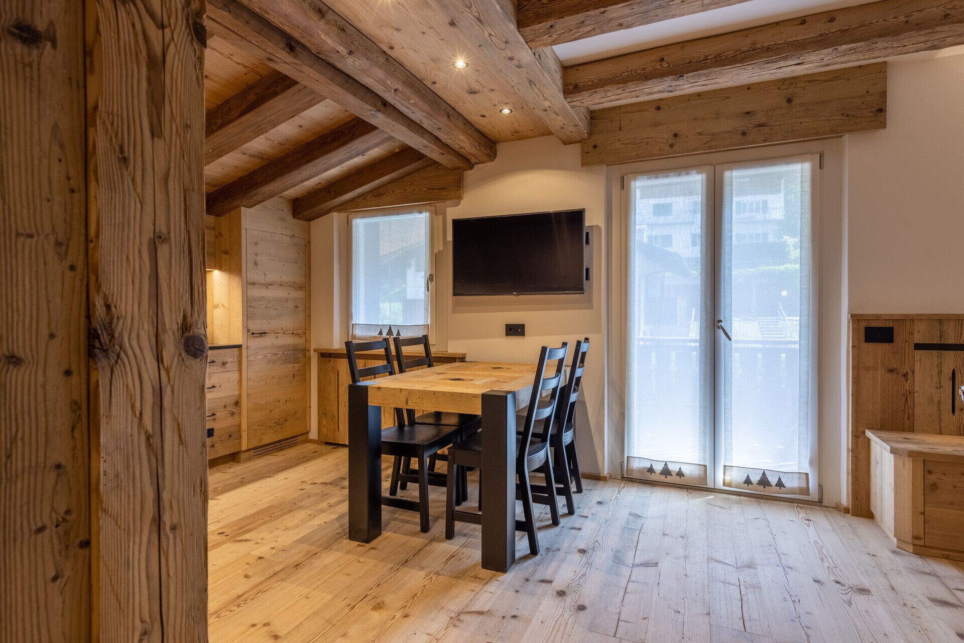 A wooden interior with a dining table, chairs, a TV, and a sliding glass door.