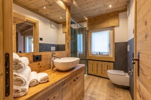 A wooden bathroom with a large mirror, a sink, and a toilet. - Lino Deluxe Suite with Wellness (Borca di Cadore)