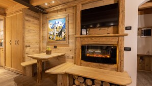 Ein gemütliches Blockhaus-Interieur mit einer hölzernen Bank, einem Kamin und einem Gemälde eines Bergdorfes.