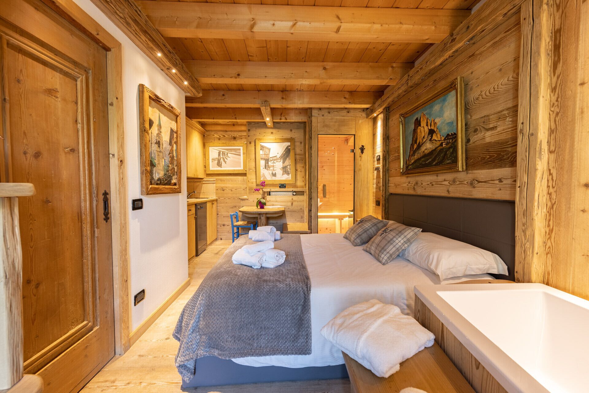 A cozy wooden room with a bed, a small table, and a sink.