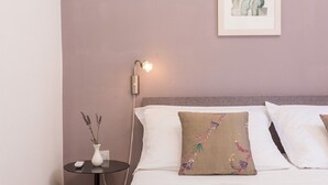 A neatly arranged hotel room with a bed, a bedside table with a vase of flowers, and a wall-mounted lamp.