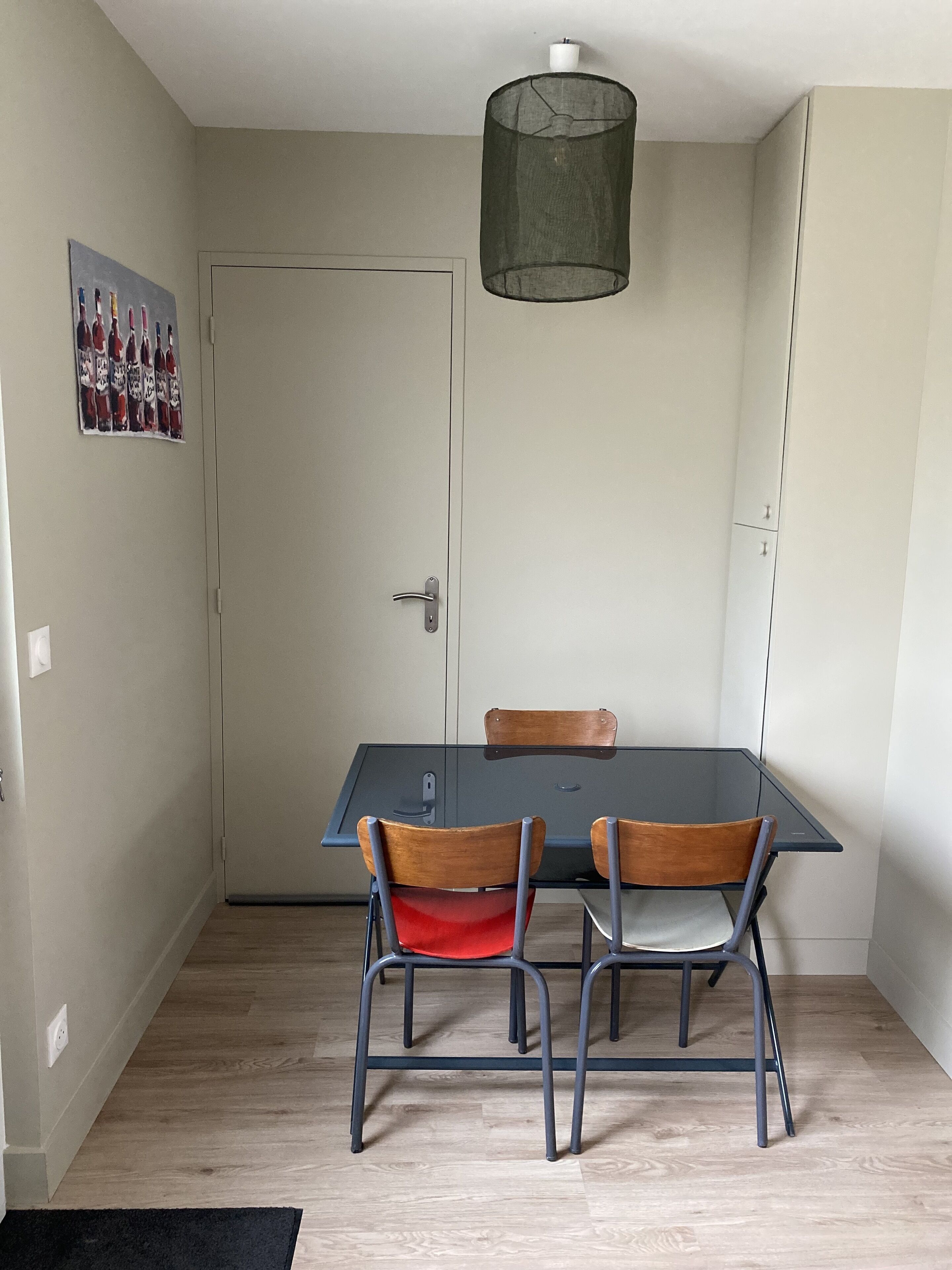 Un coin repas comprenant une table en verre, deux chaises en bois, une chaise noire, une chaise en métal et un luminaire suspendu.