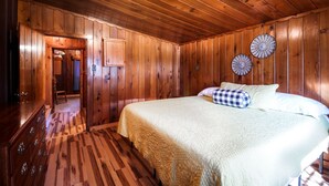 A wooden-paneled bedroom with a bed, dresser, and a mirror.