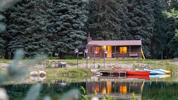 A cabin by a lake with a dock, surrounded by trees.