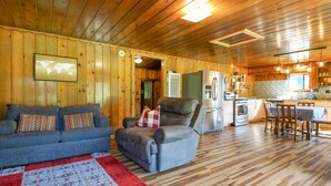 A cozy cabin interior with a wooden interior, a sofa, a chair, a dining table, and a kitchen area.