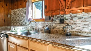A kitchen with wooden cabinets, a granite countertop, a sink, and a window with curtains.