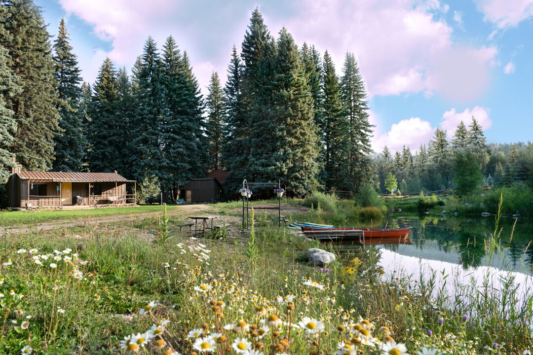 Une cabane avec une véranda, un quai avec des bateaux et un lac entouré d’arbres.