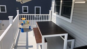 A balcony with a wooden table and chairs, a small play area with toys, and a white railing. - Adorable 2BR Condo on Long Beach Island LBI  in Ship Bottom. Beach Block! (Ship Bottom)
