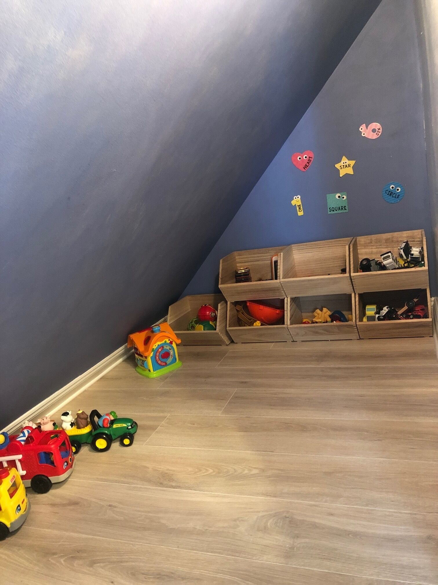 Une pièce avec un plafond en pente, des meubles de rangement en bois et un espace de jeu avec des voitures miniatures et une maison de poupée.