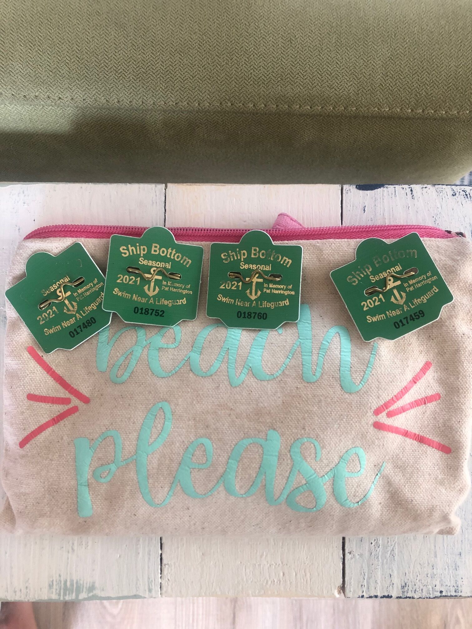 Una toalla con el texto 'beach please' bordado en color aguamarina y rosa, y tres etiquetas verdes que dicen 'Ship Bottom Seasonal 2021' y números de socorristas.