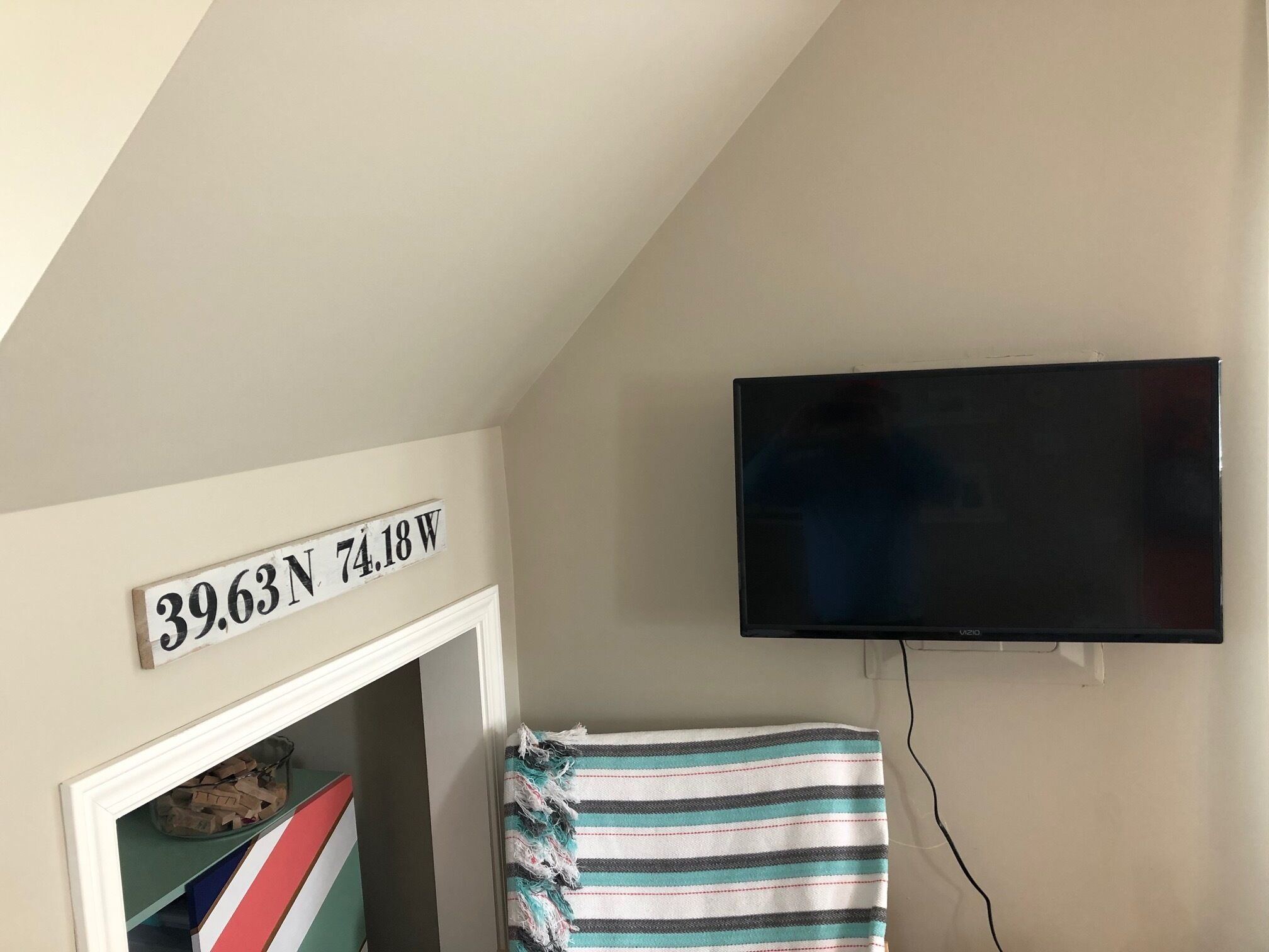 Een kamer met een aan de muur bevestigde televisie, een deur met een bordje waarop '39.63N 74.18W' staat, en een gestreepte handdoek die aan de deur hangt.