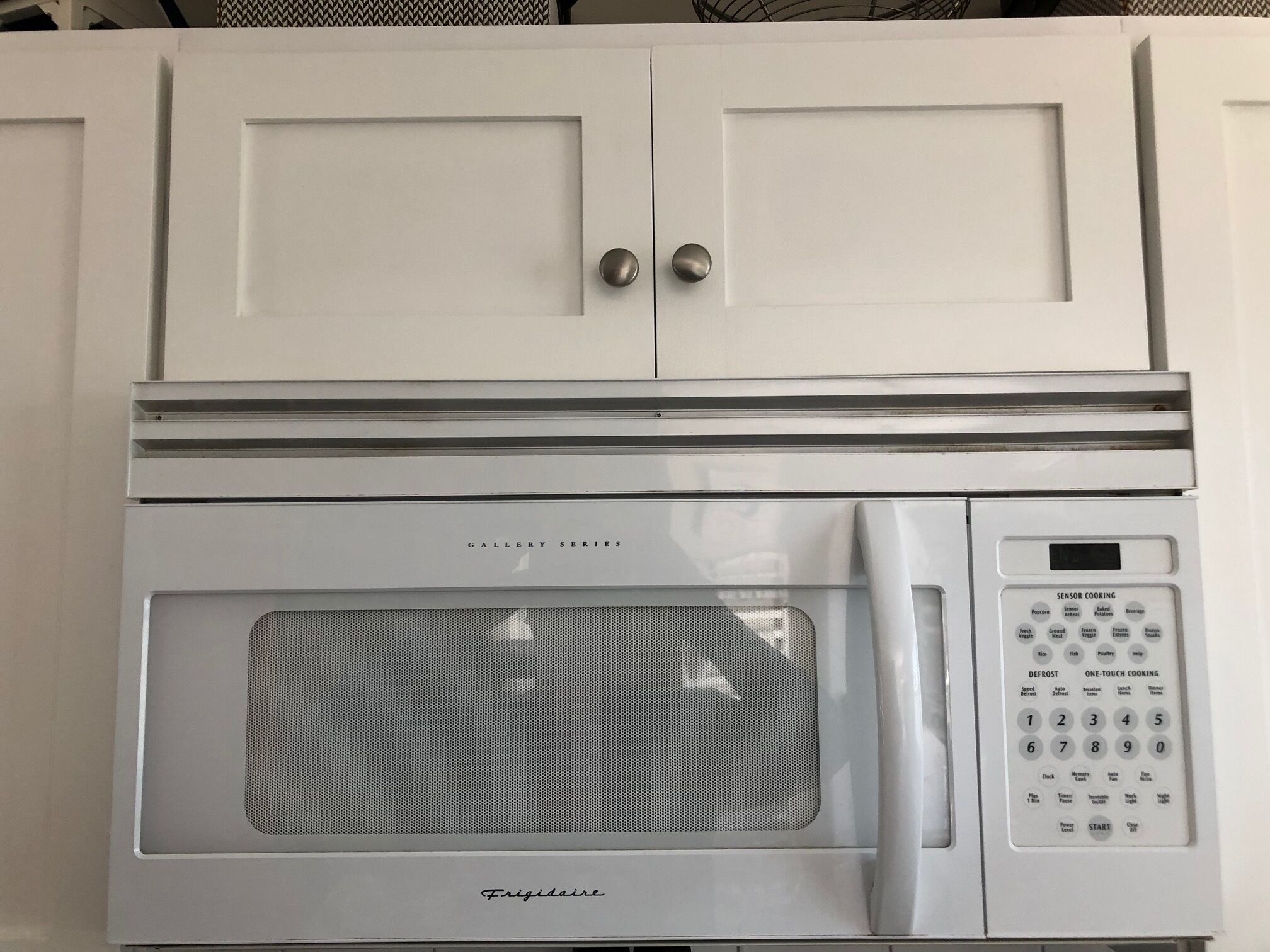 Een witte keuken met een ingebouwde magnetron en een digitaal bedieningspaneel.