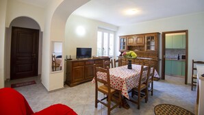 A dining area with a table set for four, wooden cabinets, a television, and a window with natural light. - Discount for the period January -May 2023 (Cala Gonone)
