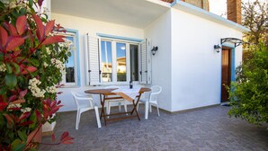 A patio with a table and chairs, a white building with blue trim, and a tiled floor. - Discount for the period January -May 2023 (Cala Gonone)