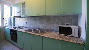 A kitchen with green cabinets, a granite countertop, a microwave, and a double sink. - Discount for the period January -May 2023 (Cala Gonone)