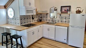 A modern kitchen with white cabinets, a microwave, a sink, and a refrigerator. There are two black stools and a window with a hexagonal design.