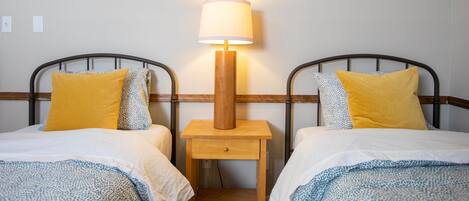 A room with two beds, each with a wooden headboard, a bedside table with a lamp, and patterned bedding.