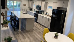 A modern kitchen with a large island, grey cabinets, and a black refrigerator.