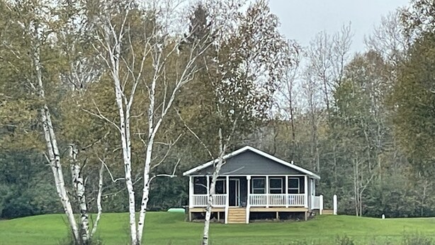 A house with a porch, surrounded by trees and a body of water.