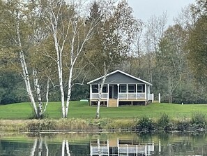 A house with a porch, surrounded by trees and a body of water. - Escanaba River Modern Retreat • 10 Min to Town (Gladstone)