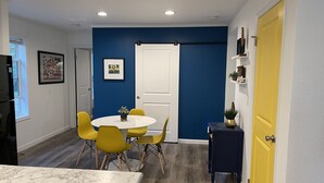 A compact kitchen with a marble countertop, a dining area with yellow chairs, and a blue accent wall.
