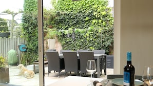 A dining area with a table set for two, a bottle of wine, and a glass. Outside, a dog is visible through a glass door.