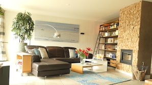 A living room with a sectional sofa, a coffee table, a fireplace, a bookshelf, and a large plant.