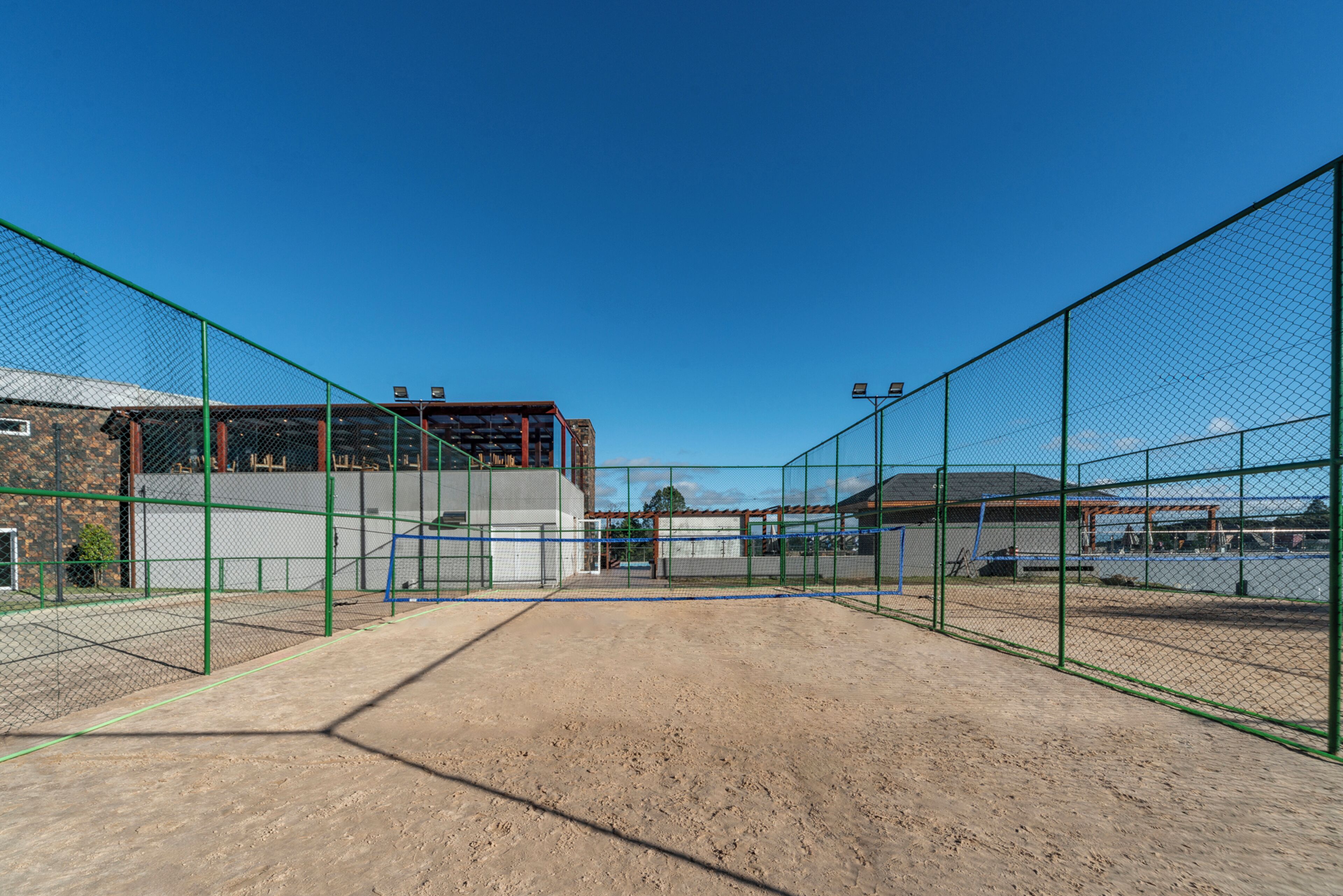 A tennis court with a net, surrounded by green fencing, and buildings in the background.