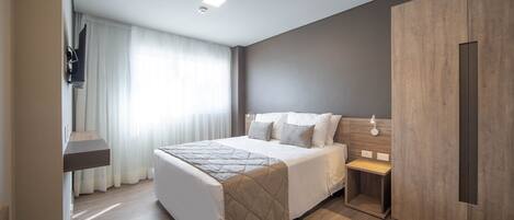 Una habitación de hotel moderna con una cama grande, una mesita de noche, un armario y un televisor instalado en la pared.