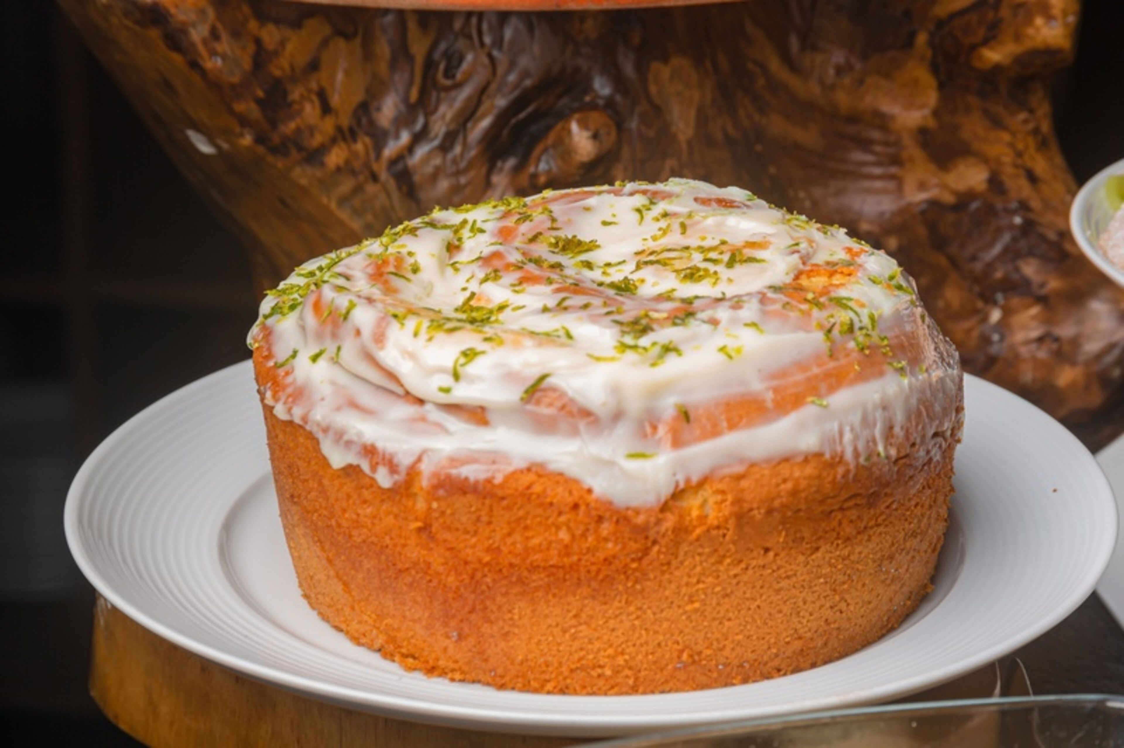 A round cake with white icing and green garnish on a white plate.